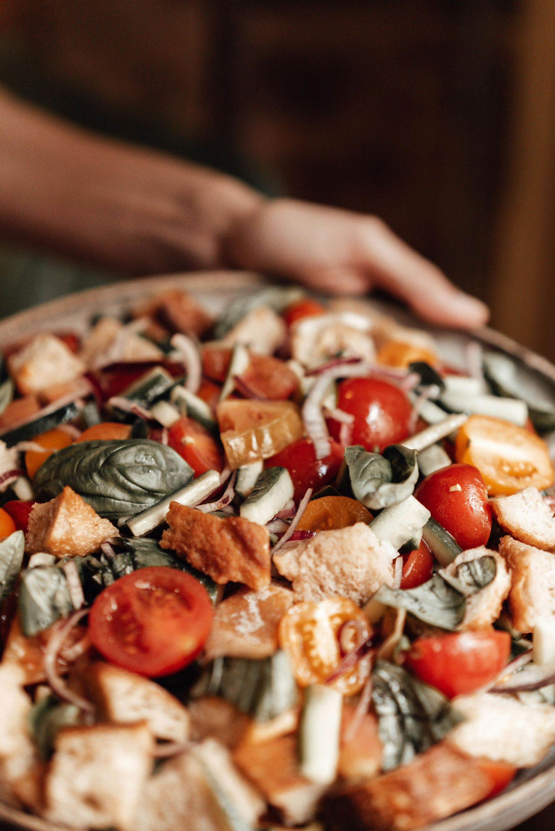 A person is holding a plate of salad with tomatoes and croutons.