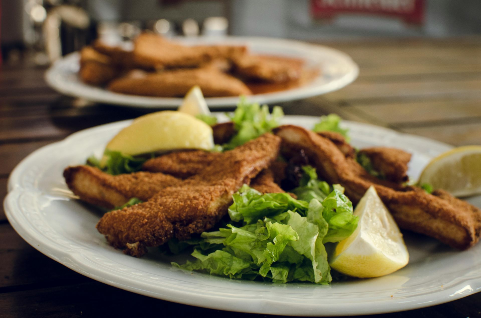 A white plate topped with fried fish and lettuce on a wooden table.