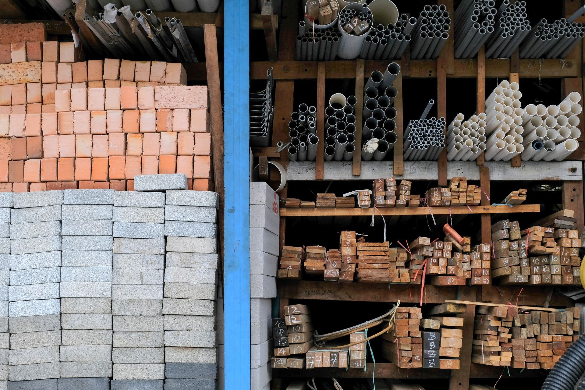 Shelves with stacked bricks, lumber, and assorted metal and PVC pipes in storage.