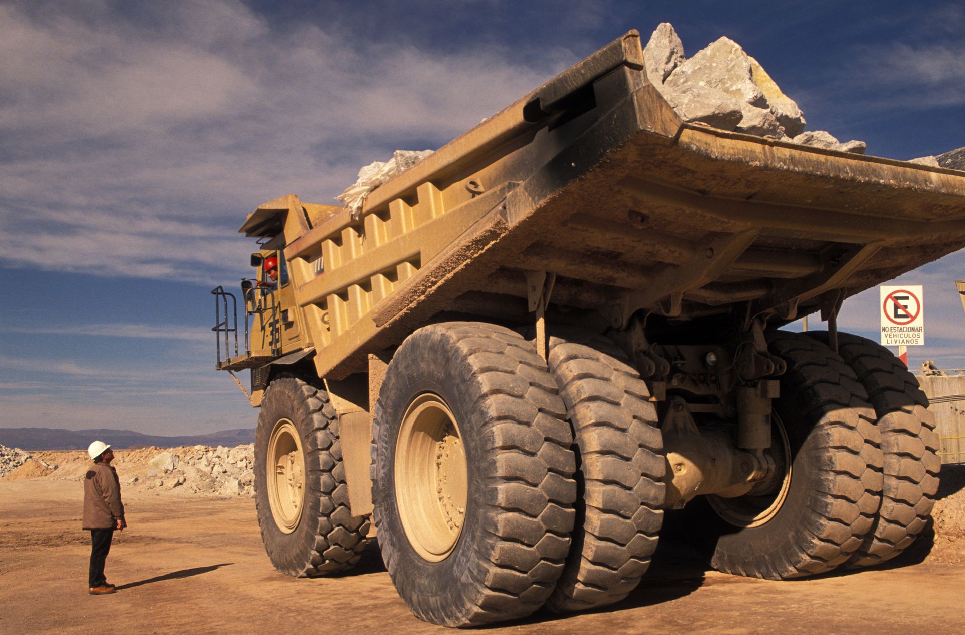 Giant mining haul truck loaded with ore next to worker at open-pit mine in South America.
