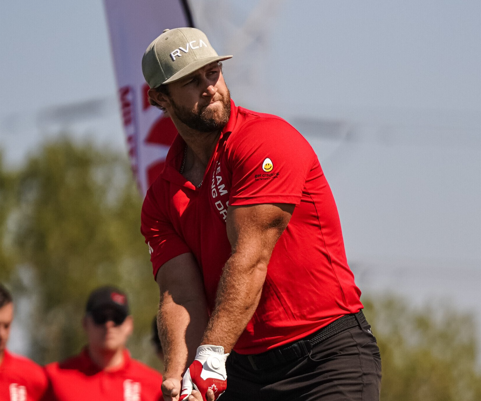 A man in a red shirt is swinging a golf club on a golf course.