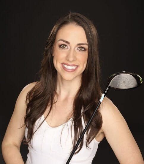 A woman in a white tank top is holding a golf club