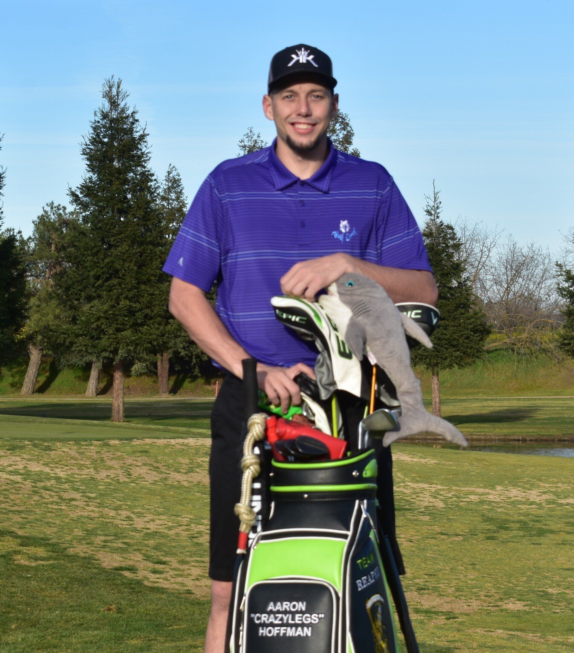 A man in a purple shirt is holding a golf bag