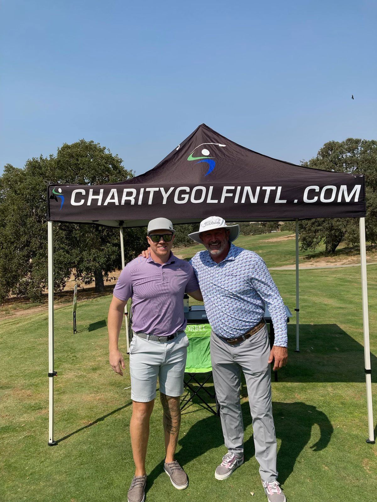 Two men are posing for a picture in front of a charity golf tent.