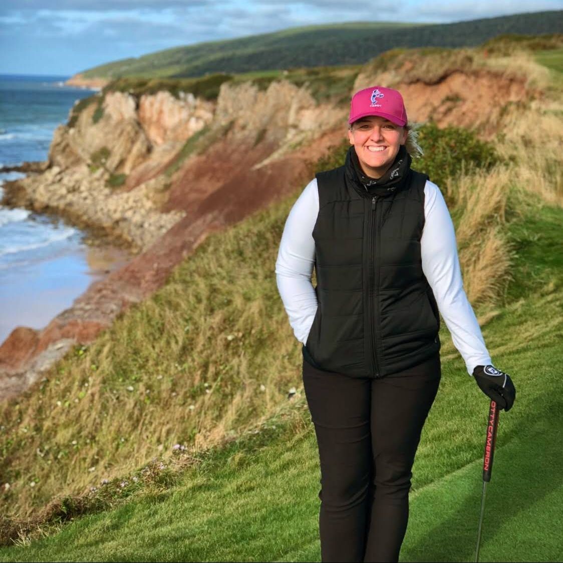 A woman in a pink hat is standing on a golf course holding a golf club.