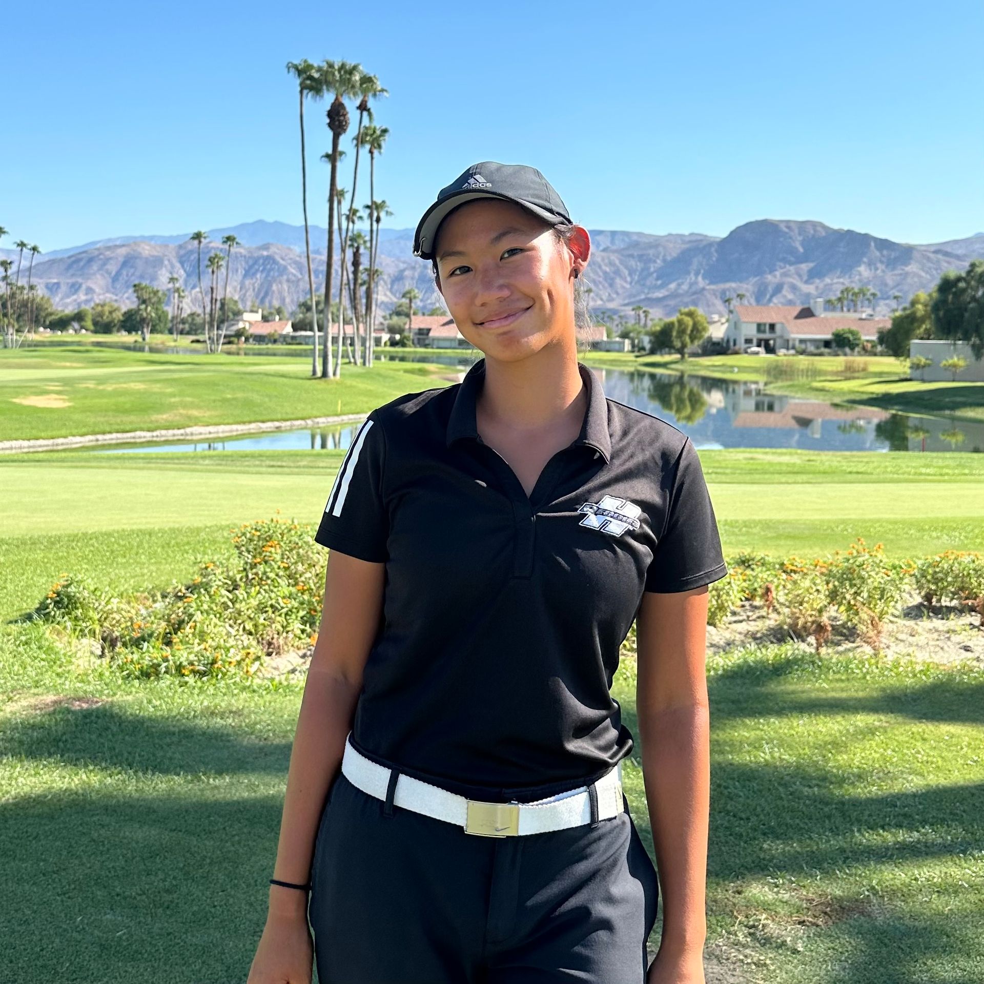 Woman in golf attire on a golf course with mountains in the background.