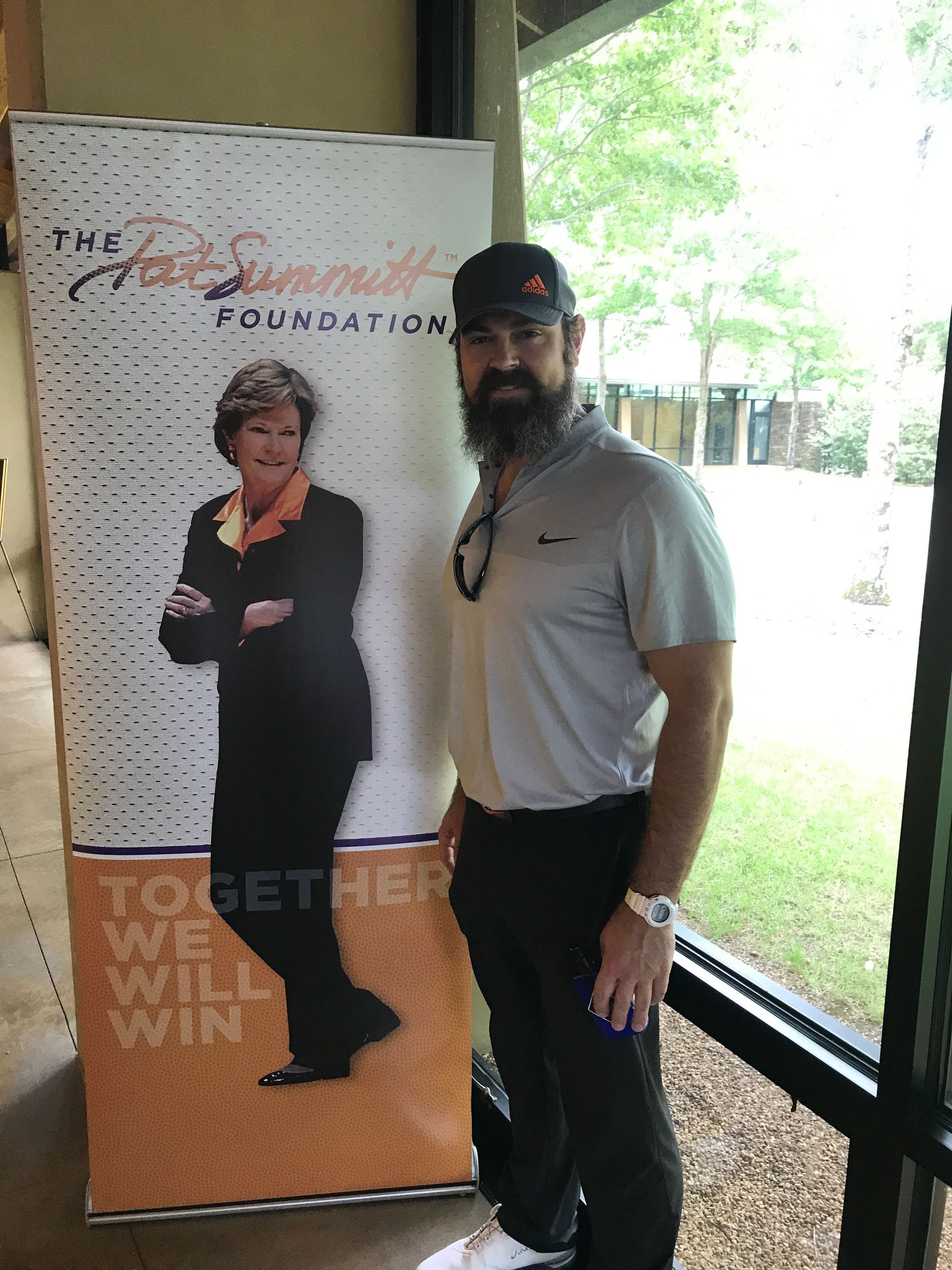 Man with beard stands by a banner for The Pat Summitt Foundation; outside setting.
