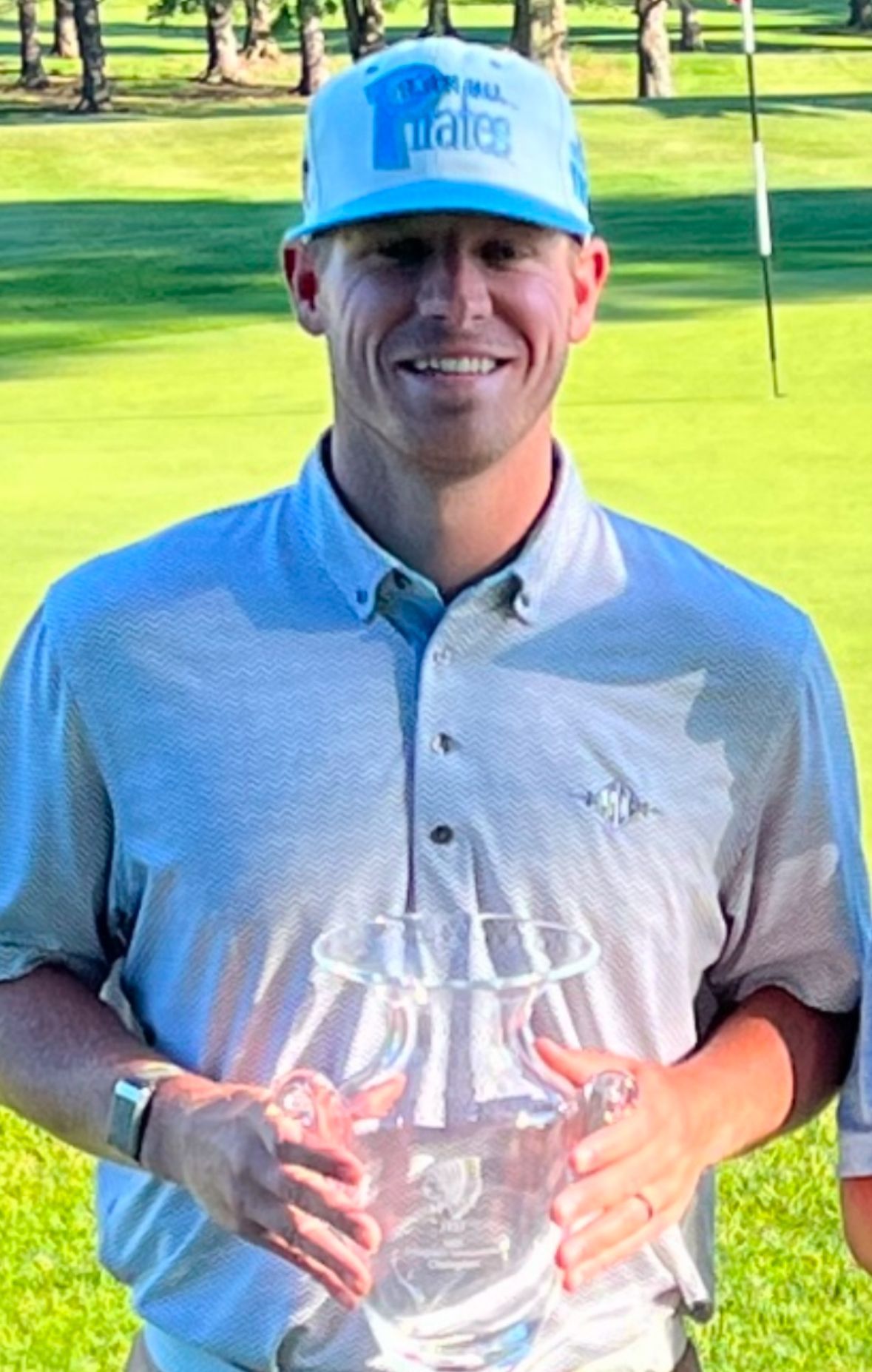 A man in a blue hat is holding a trophy on a golf course.