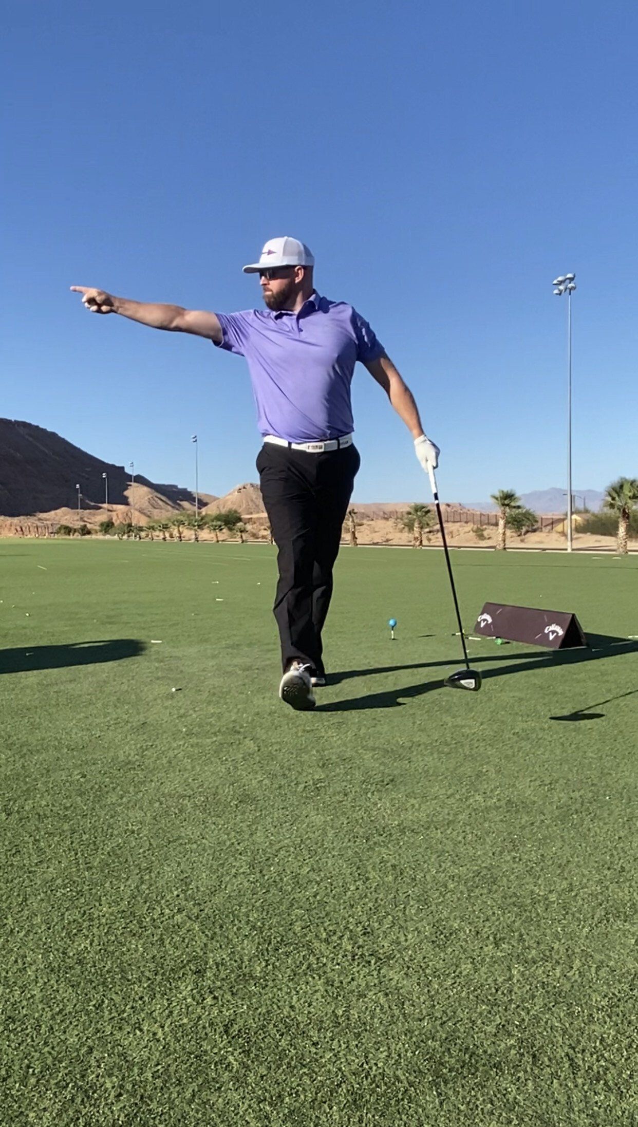 A man is standing on a golf course holding a golf club and pointing.