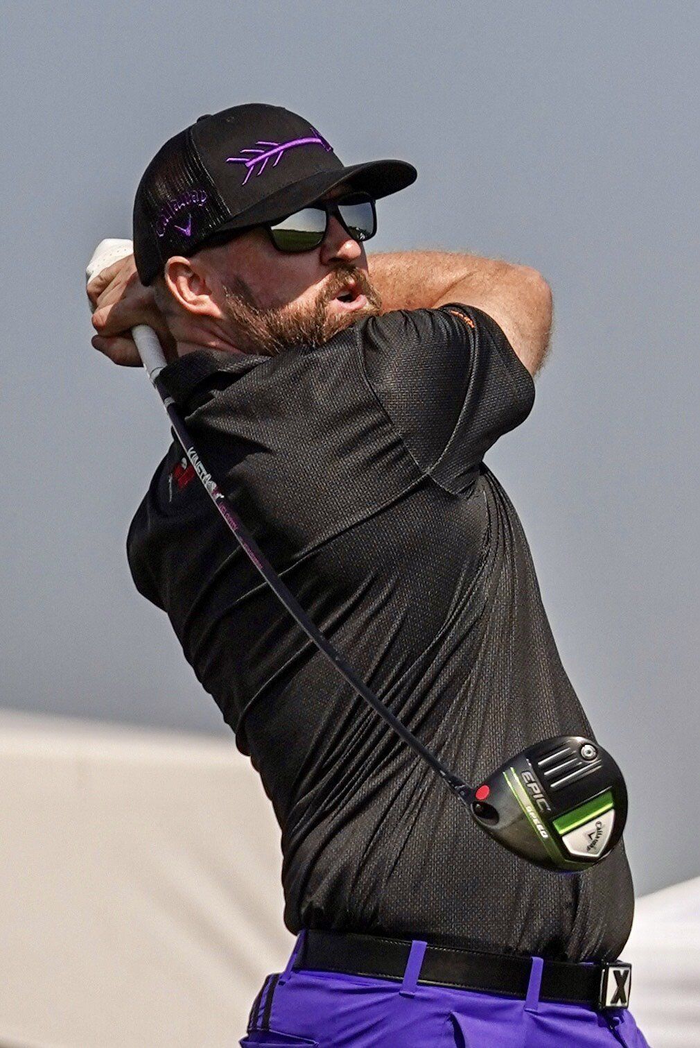 A man in a black shirt and purple pants is swinging a golf club.