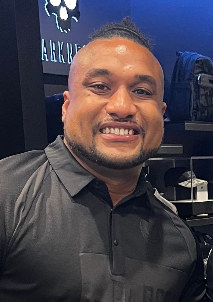 Man with a mohawk smiling in a store, wearing a dark shirt.