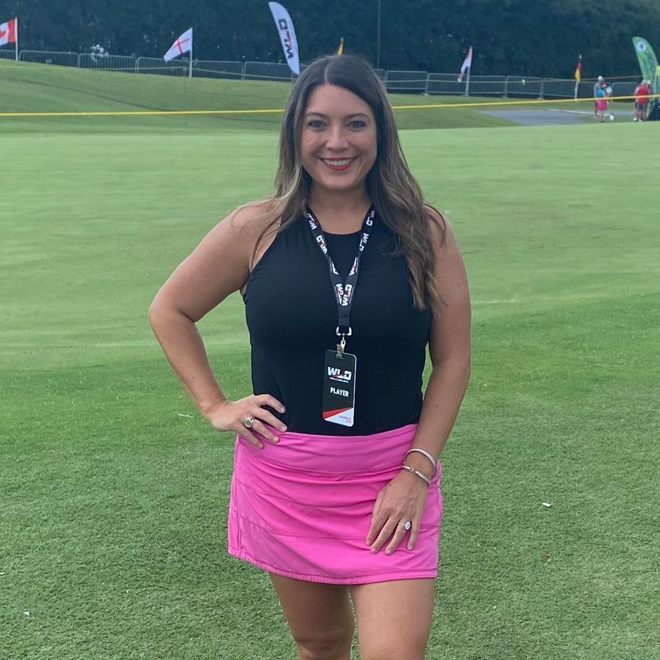 A woman in a black top and pink skirt is standing on a golf course.
