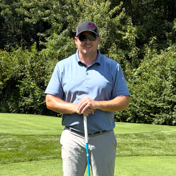 A man wearing a hat and a blue polo smiles for the camera with golf club in hand