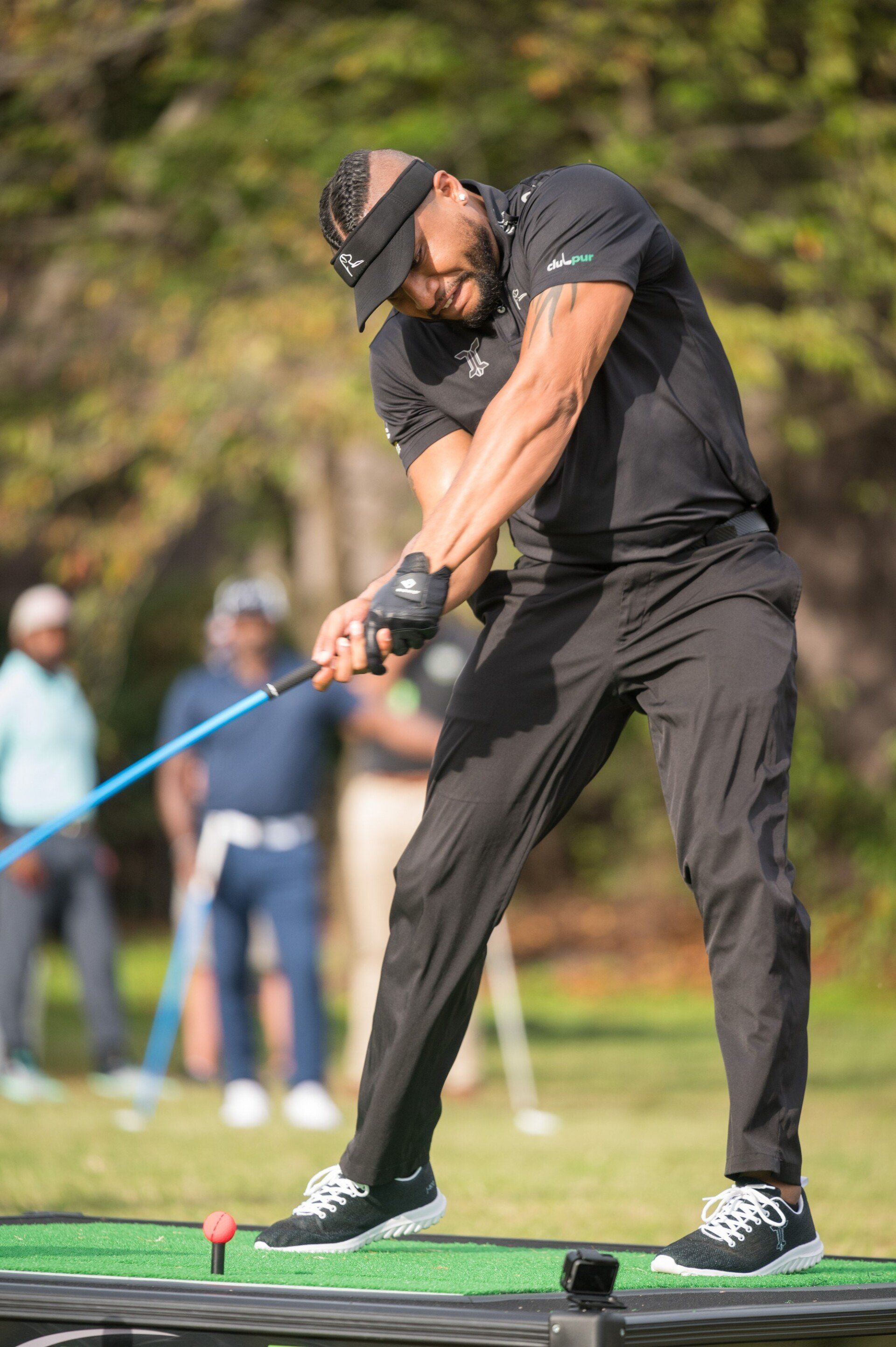 Golfer in black outfit swinging club on a green course.