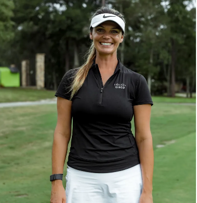 Woman in black shirt and white visor smiling on a golf course, wearing a smartwatch.