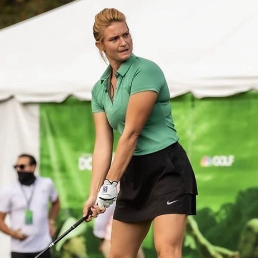 A woman in a green shirt and black skirt is swinging a golf club