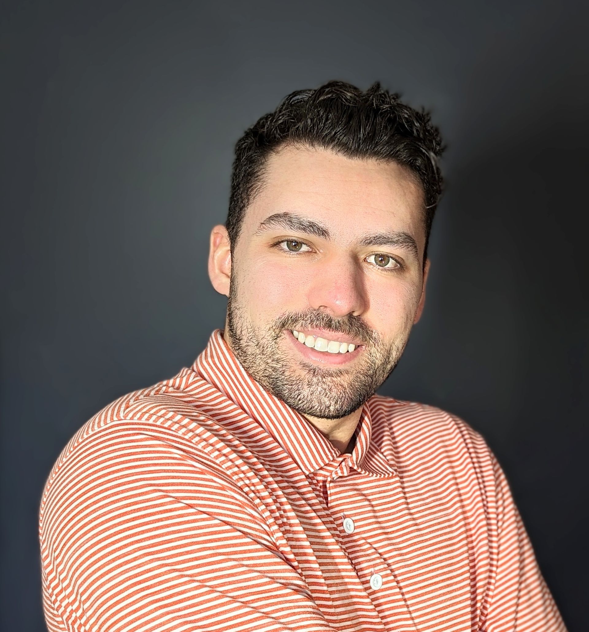 A man with a beard is wearing a red and white striped shirt and smiling for the camera.