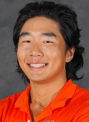 A young man wearing an orange shirt is smiling for the camera.