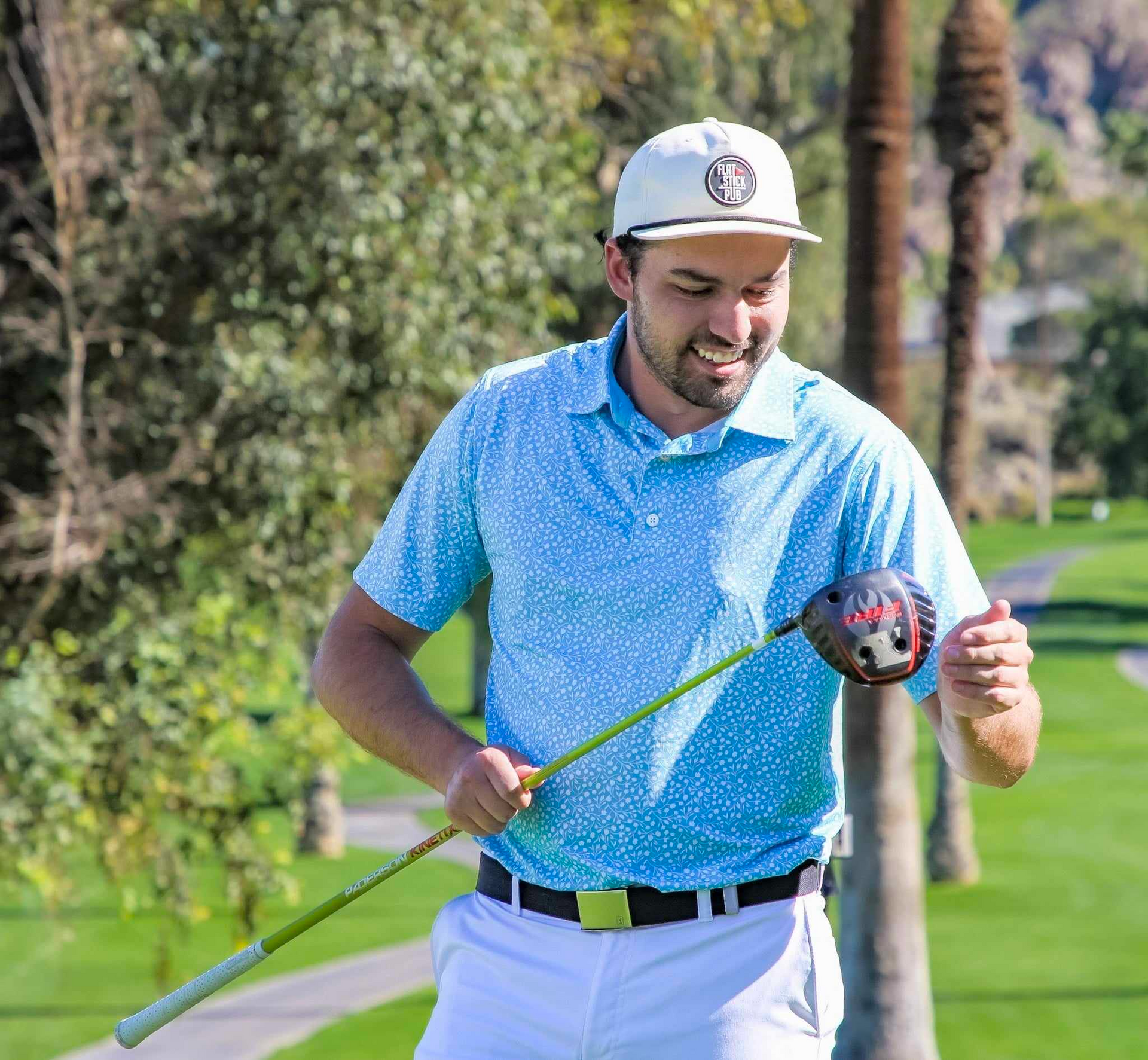 Man holding a golf club with a golf course in the background, smiling.