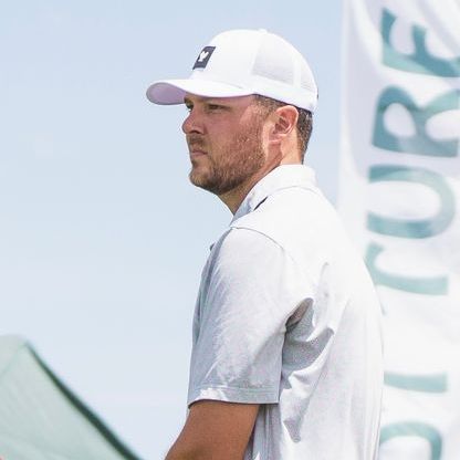 A man wearing a white hat and a gray shirt is standing in front of a flag that says picture.