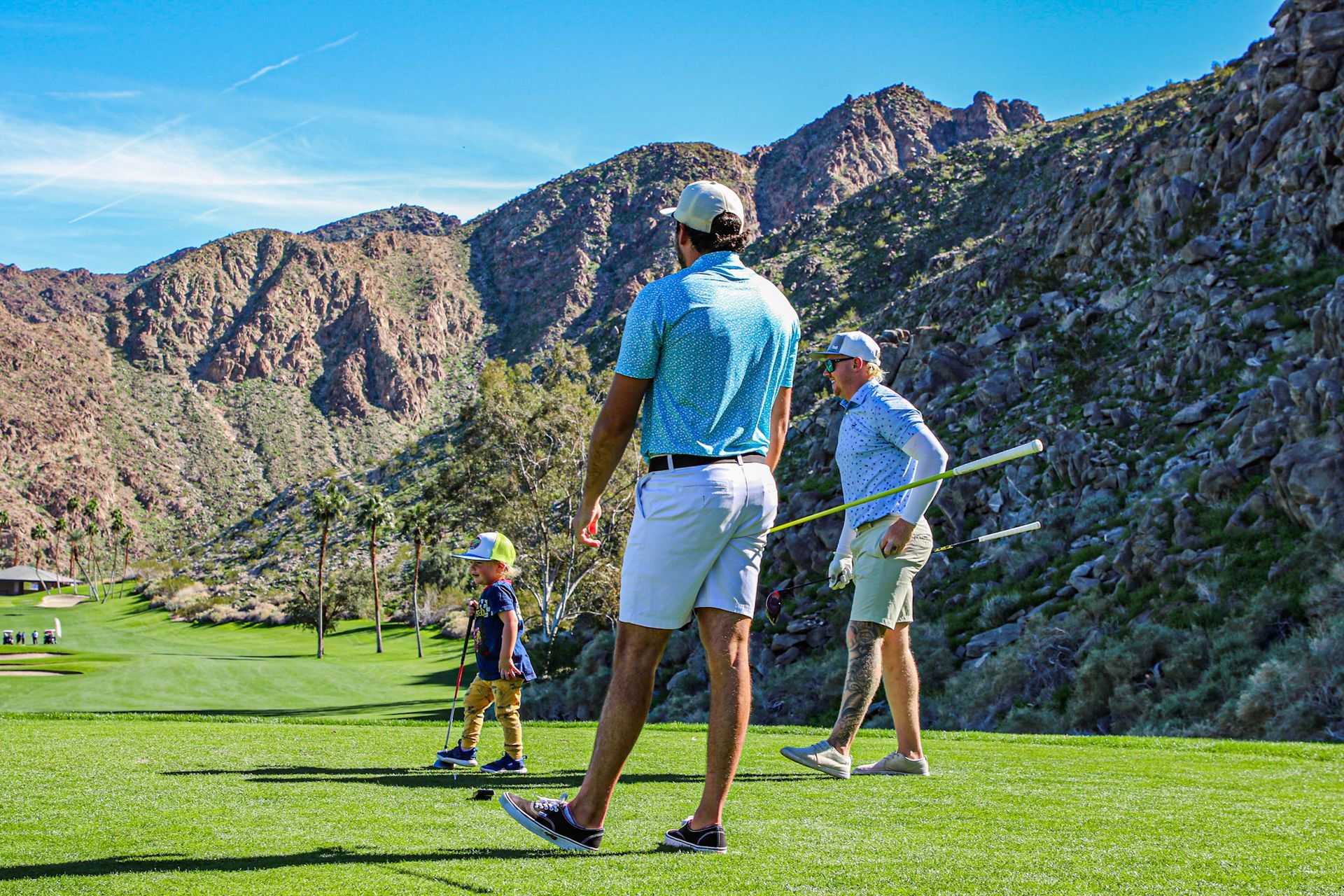 People golfing on a green course with mountains in the background. Sunny day.