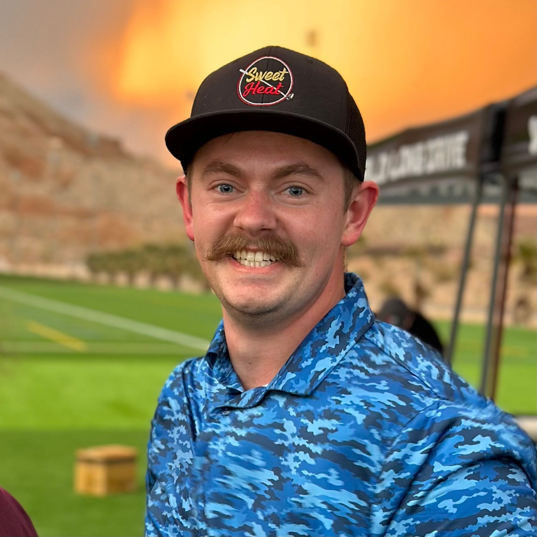 A man with a mustache is wearing a hat and a blue shirt.