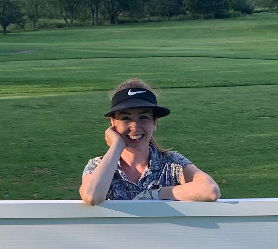 A woman wearing a hat and visor is leaning over a white fence.