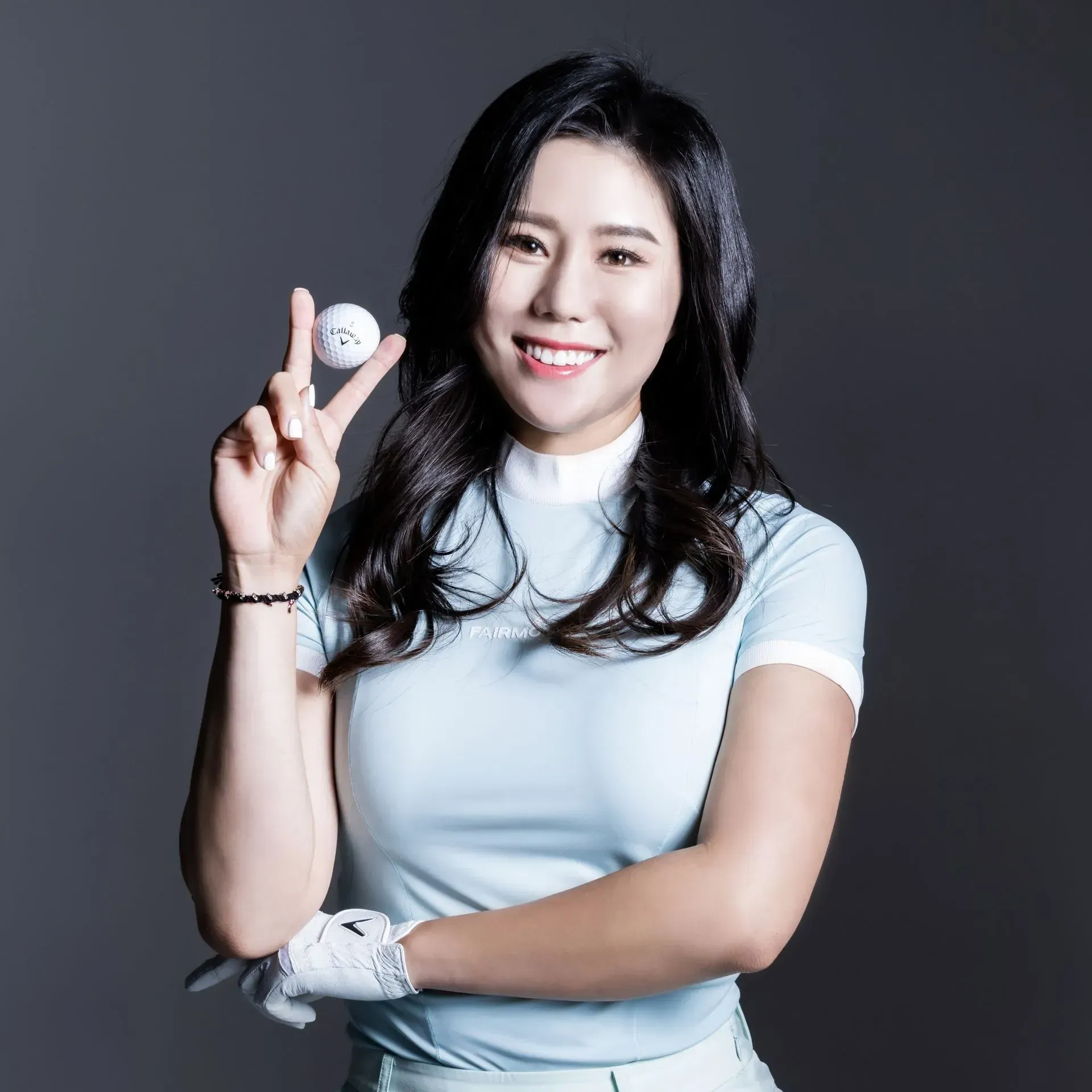 Woman in light blue golf attire holding a golf ball, smiling.