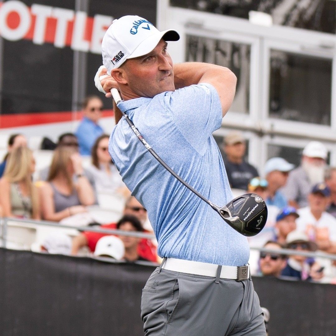 A man in a blue shirt and white hat is swinging a golf club