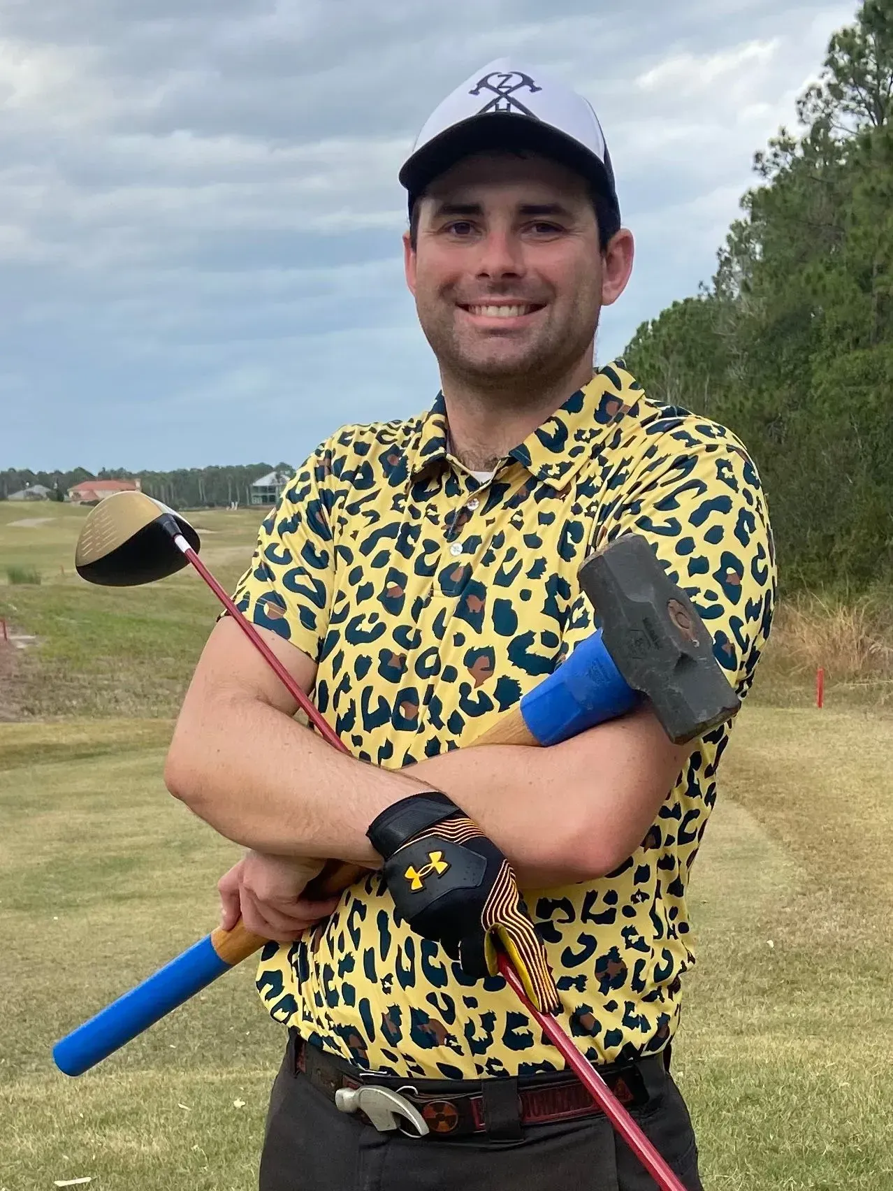 A man in a leopard print shirt is holding a golf club and a hammer.
