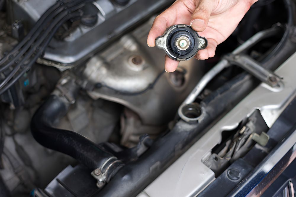 A Person Is Holding A Radiator Cap Over A Car Engine — Antons Recycling In Ciccone, NT