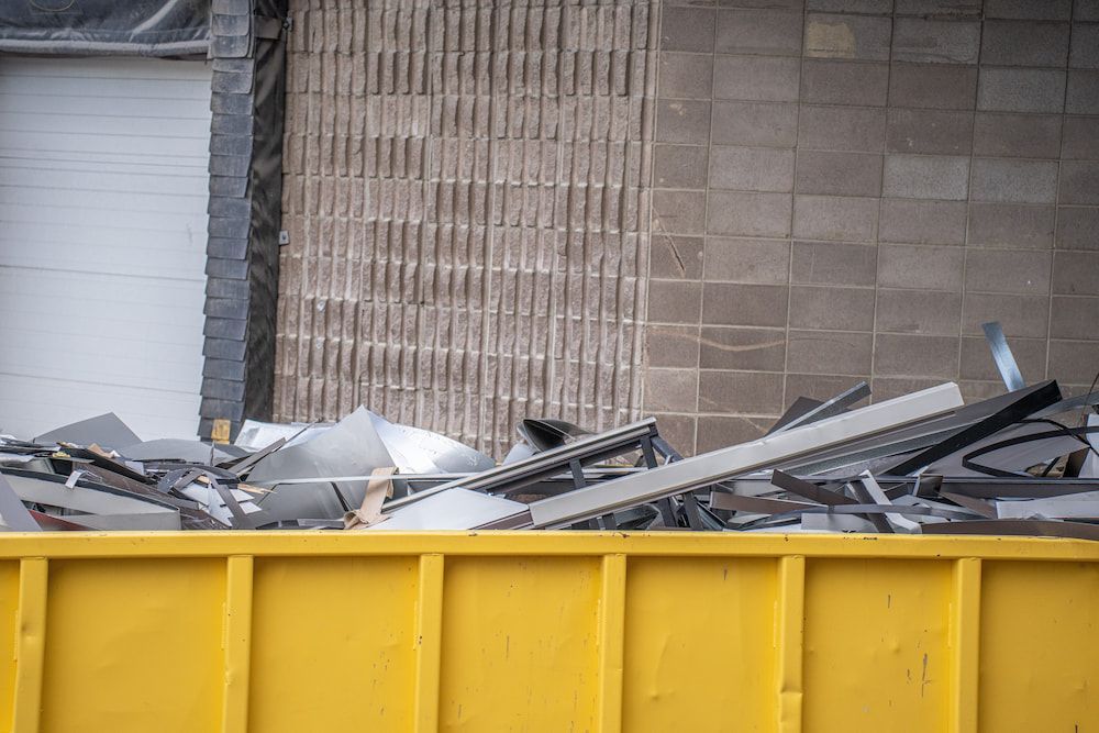 A Yellow Dumpster Filled With Scrap Metal In Front Of A Building — Antons Recycling In Ciccone, NT
