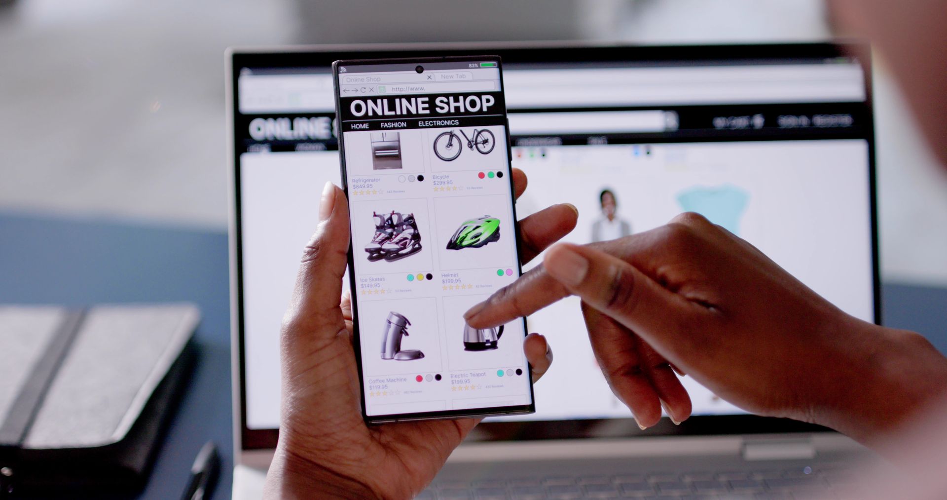 Person shopping on a website with a smartphone, with a laptop in the background.