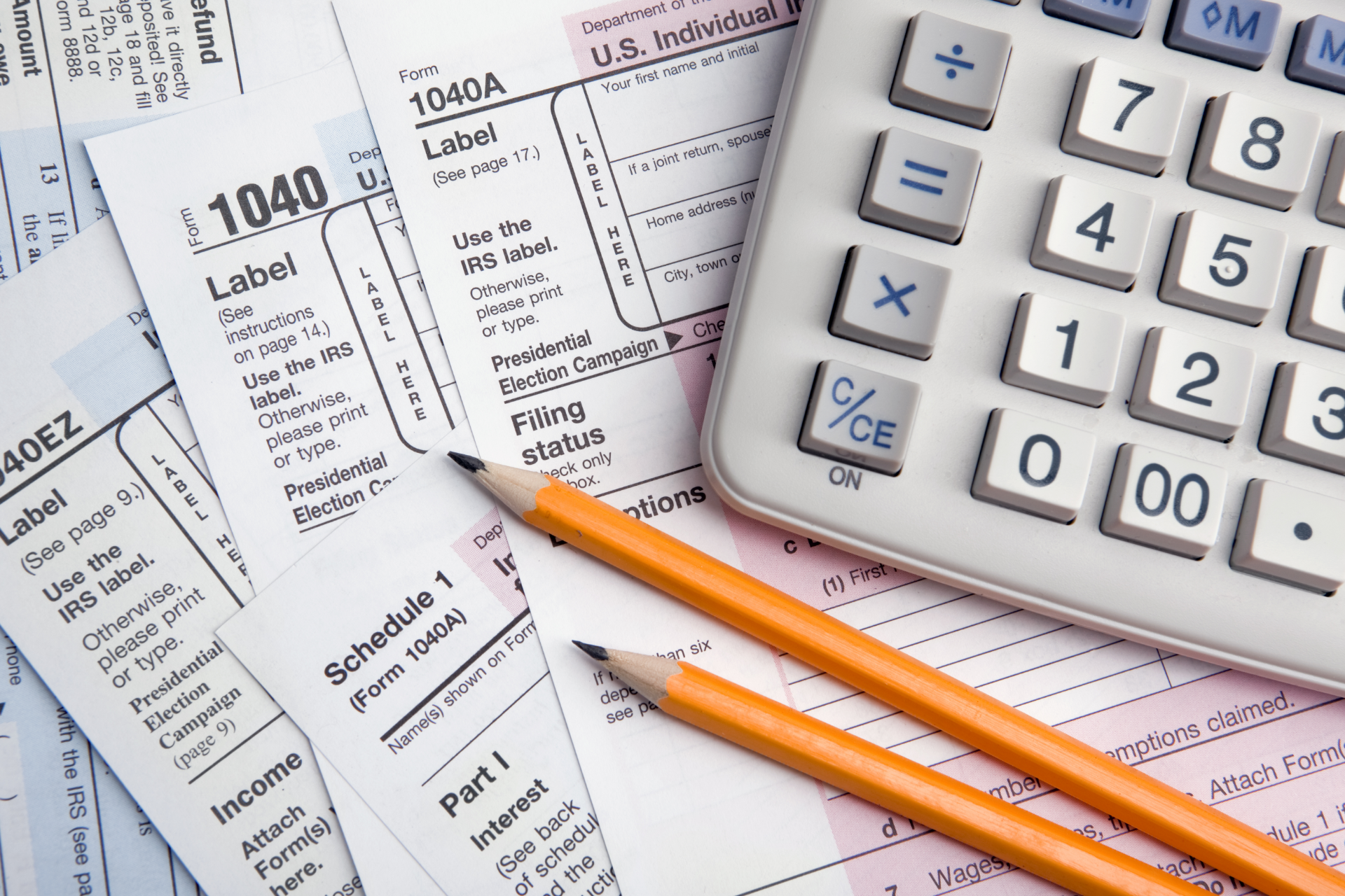 Tax forms with orange pencils and a calculator on a desk