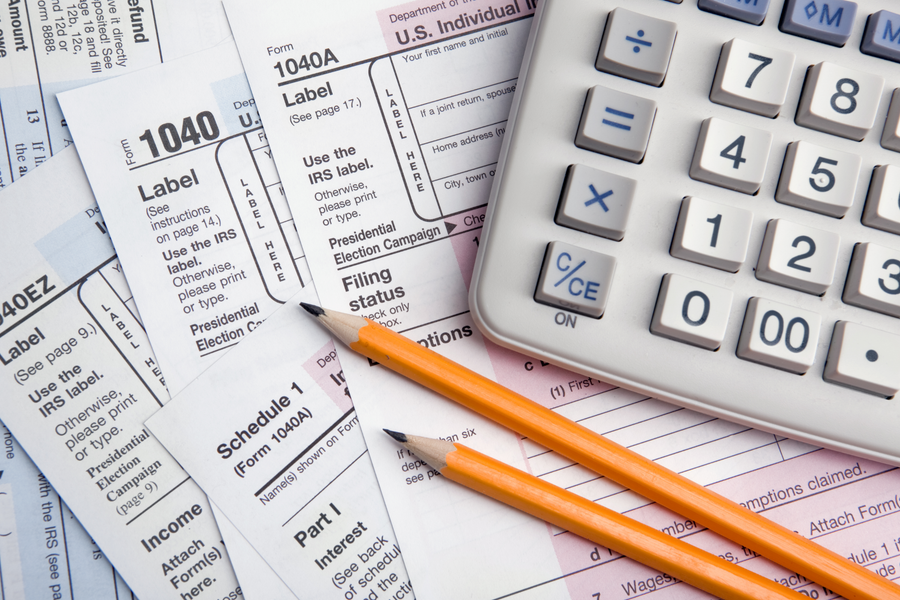 Tax forms with orange pencils and a calculator on a desk