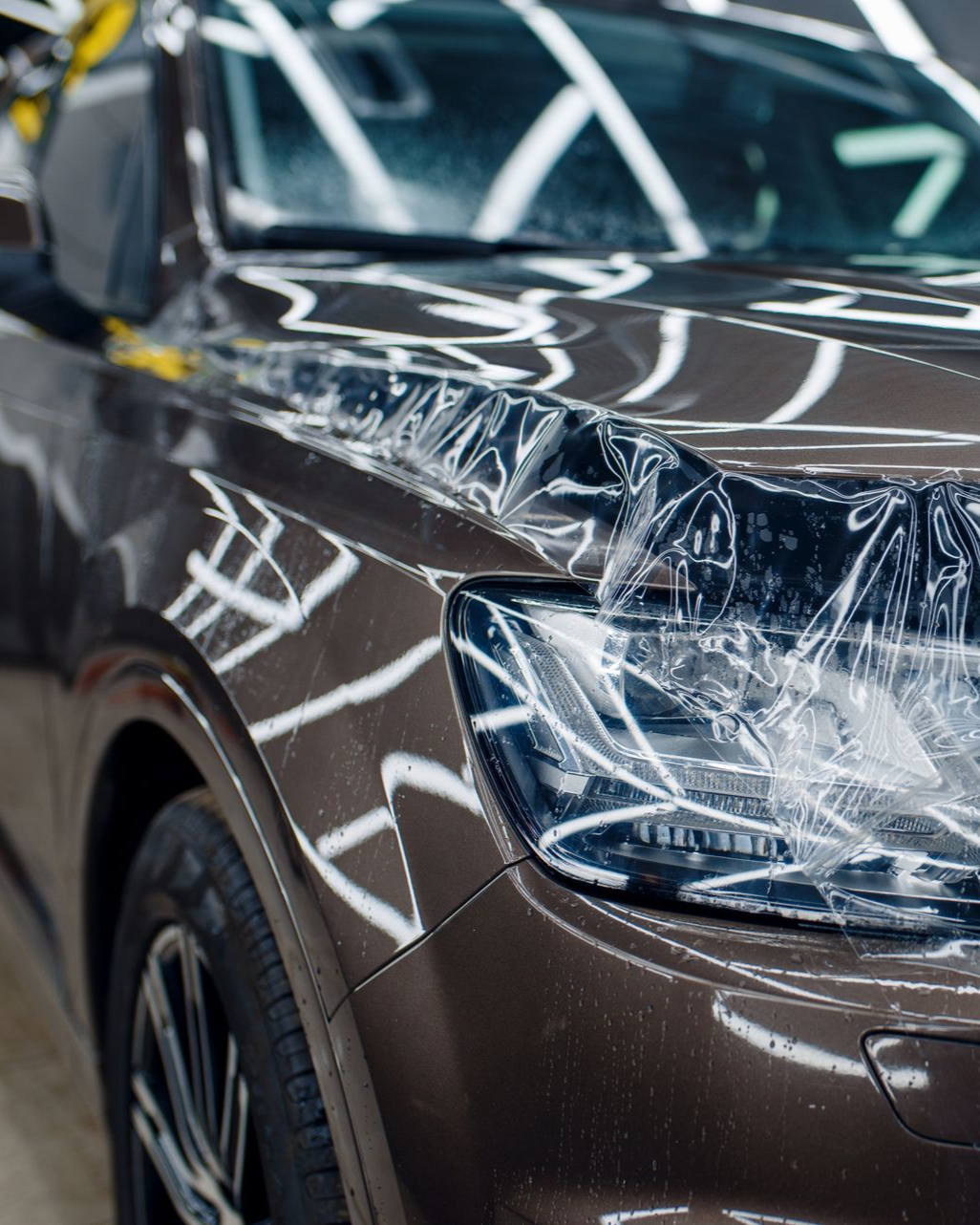 Brown car wrapped in protective plastic film inside a showroom