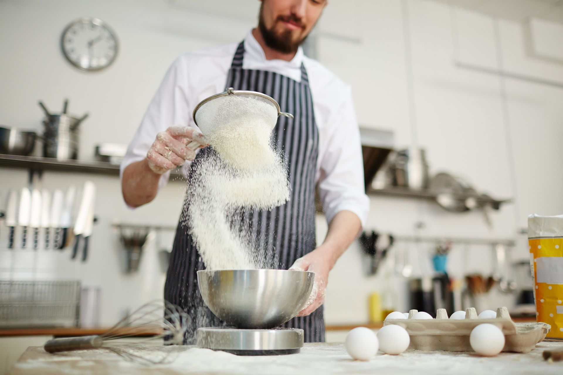 Un hombre está tamizando harina en un bol en una cocina.