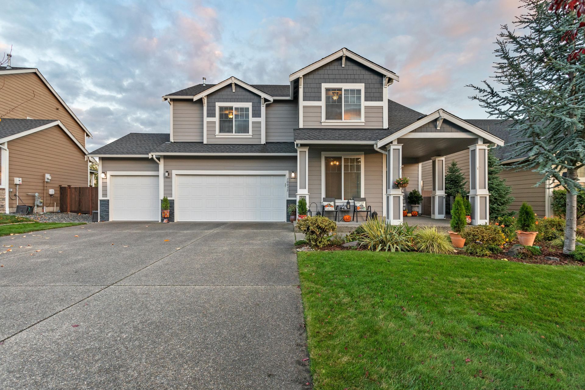 Two-story suburban house with a three-car garage, front porch, driveway, and manicured lawn