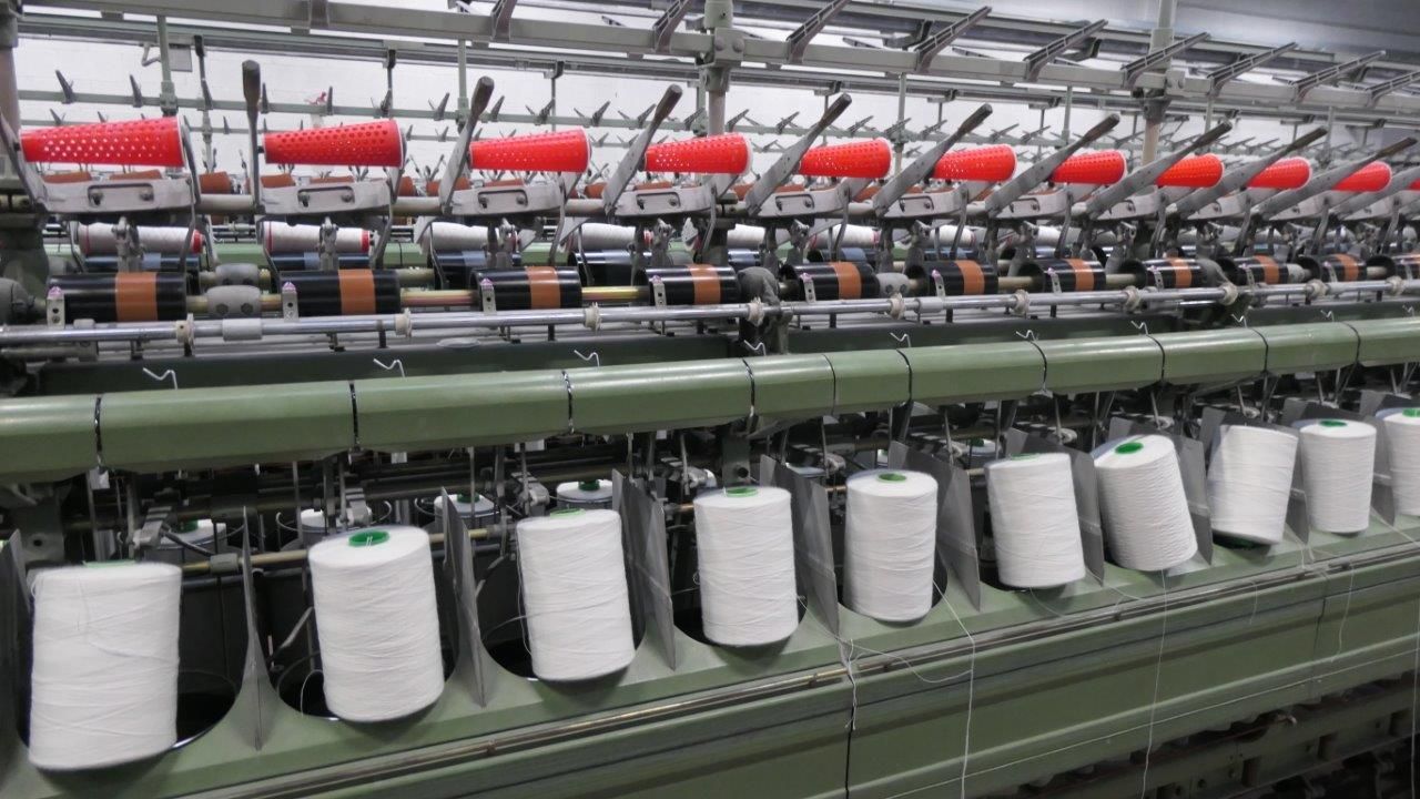 Macchinario tessile industriale con file di rocchetti di filato bianco 