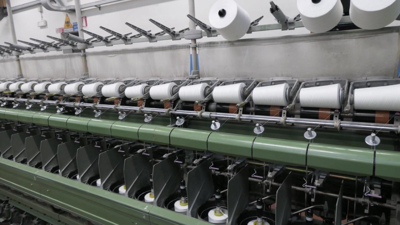 All'interno di una fabbrica, una macchina per la filatura tessile con numerose bobine 