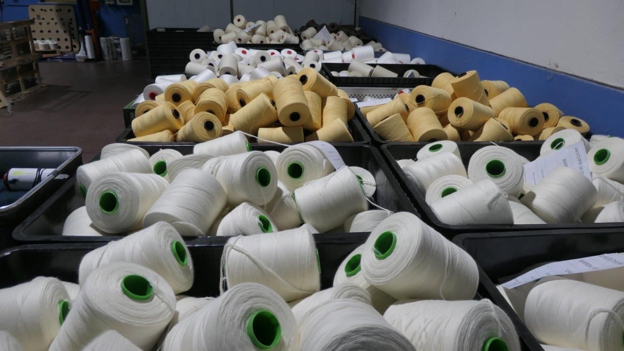 In un magazzino, contenitori neri pieni di rocchetti di filo bianco e giallo chiaro.