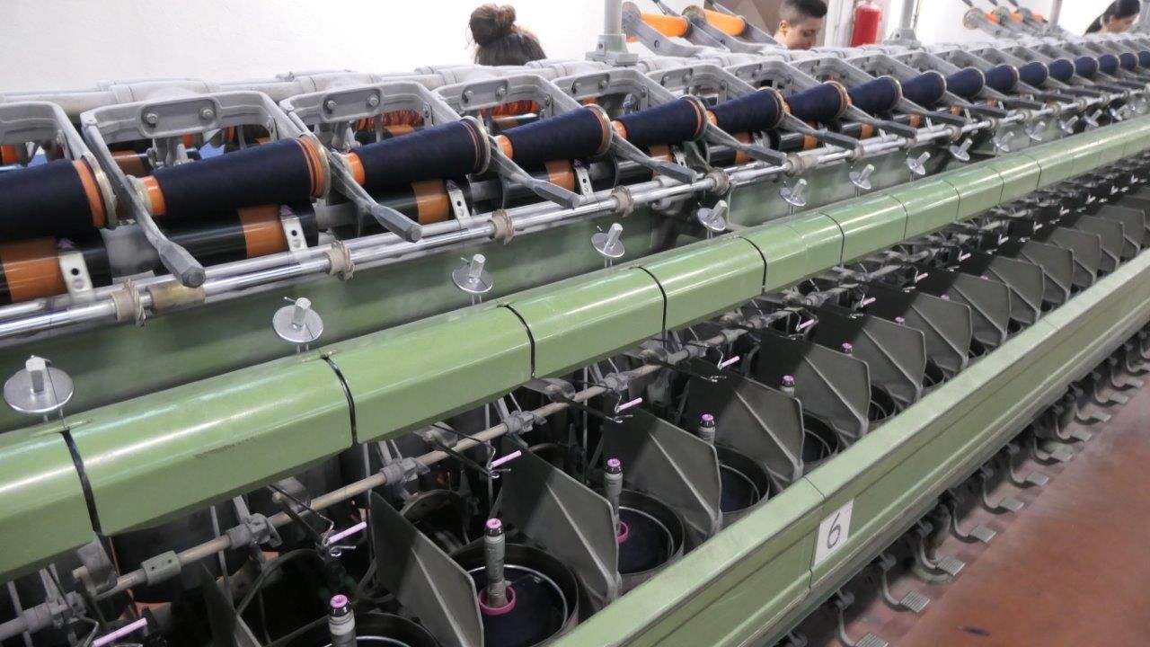 Macchina per filatura industriale che lavora filato blu scuro su più bobine in un ambiente di fabbrica.
