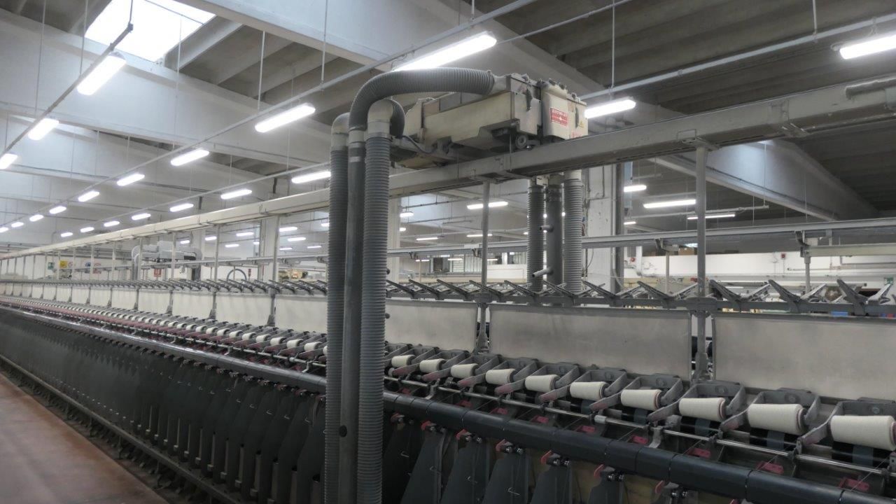Una lunga macchina automatizzata per la filatura tessile in un luminoso ambiente industriale.