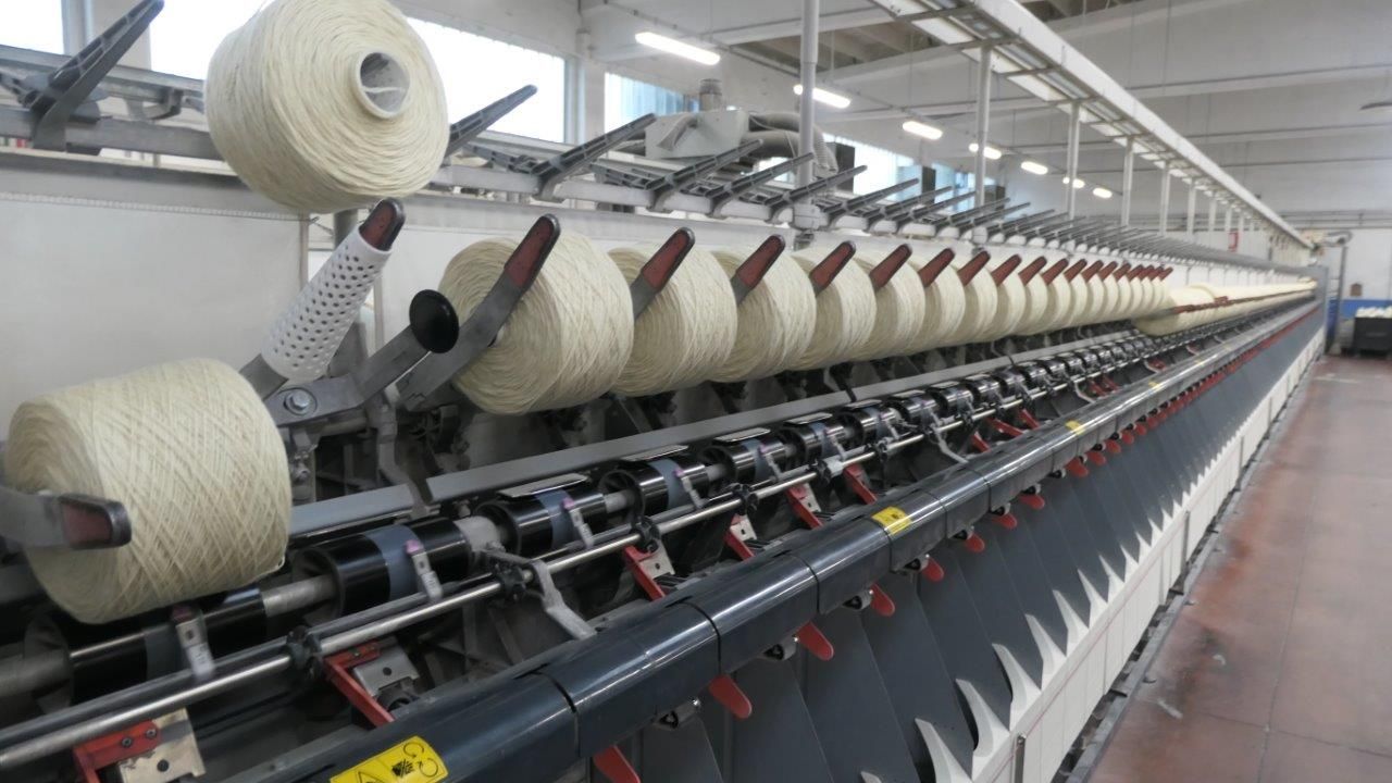 Una lunga fila di rocchetti di filato bianco montati su una grande macchina per filare industriale in una fabbrica.