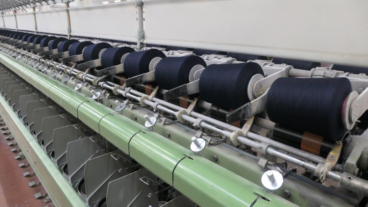 Una fila di bobine di filato scuro su una macchina per la filatura tessile industriale in una fabbrica.