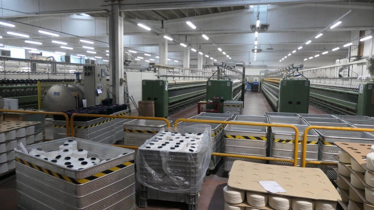 Il reparto industriale di una fabbrica tessile presenta file di macchinari verdi per la filatura