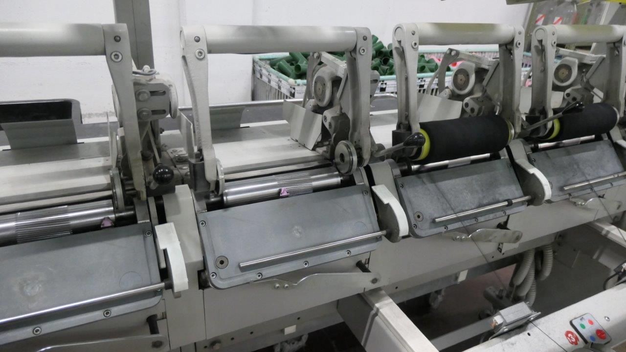 In uno stabilimento tessile, una fila di macchine industriali per l'avvolgimento del filato, con bobine nere di filo.