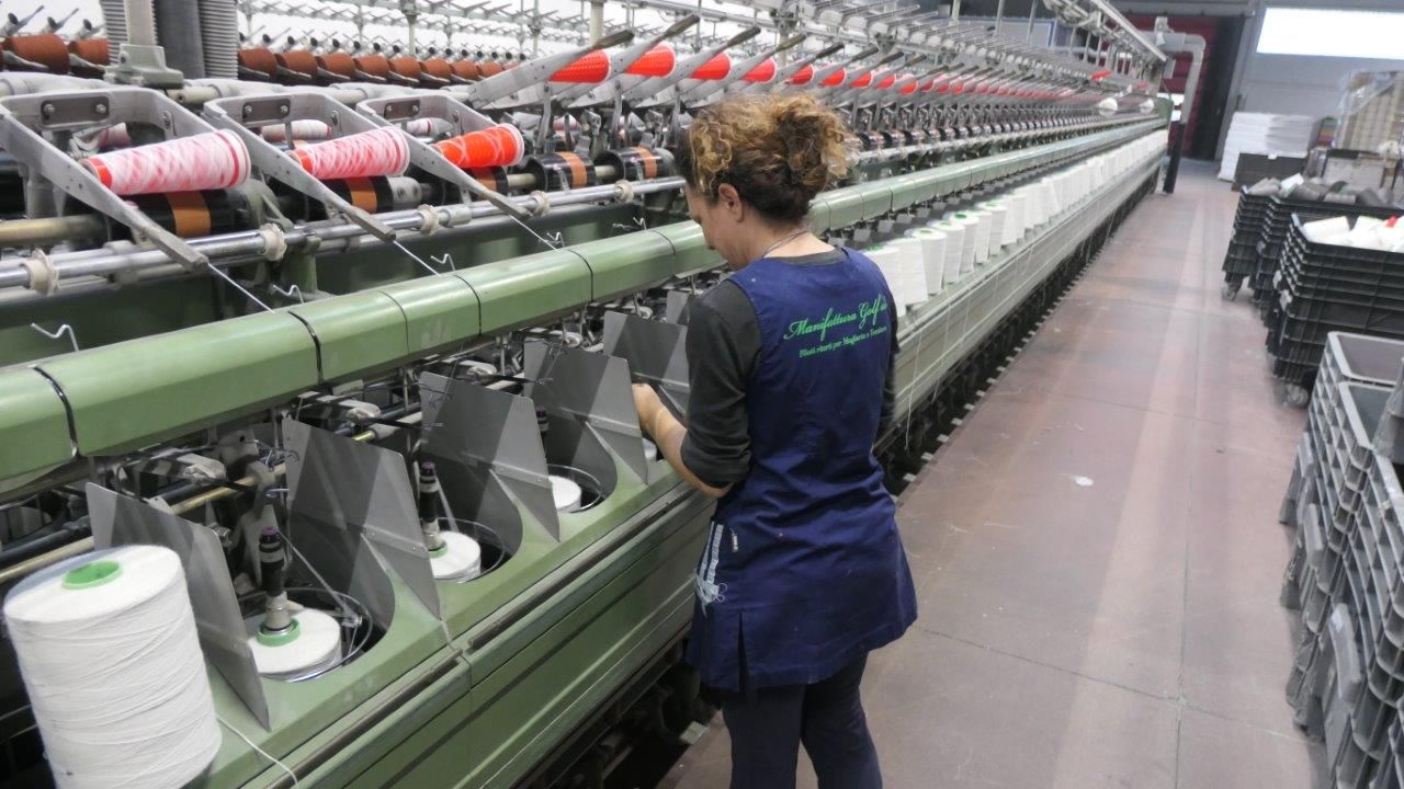 In un ambiente di fabbrica, un operaio sorveglia una lunga macchina per la filatura industriale con file