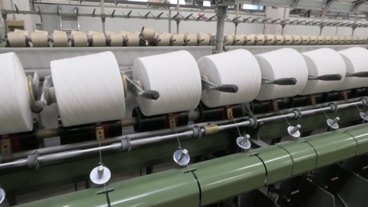 Una fila di grandi bobine di filato bianco montate su una macchina per la produzione tessile in un ambiente industriale.
