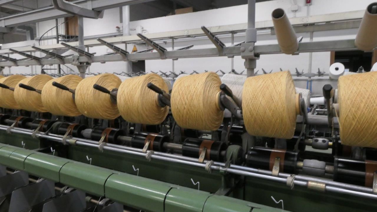 Una fila di bobine con filato conciato avvolto, montate su una macchina per la produzione tessile in una fabbrica.